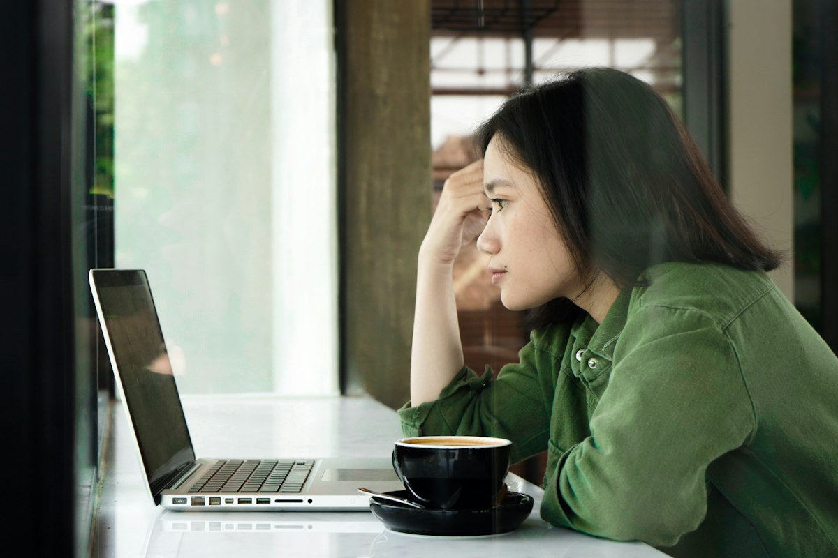 カフェでノートパソコンを前に考えごとをする女性