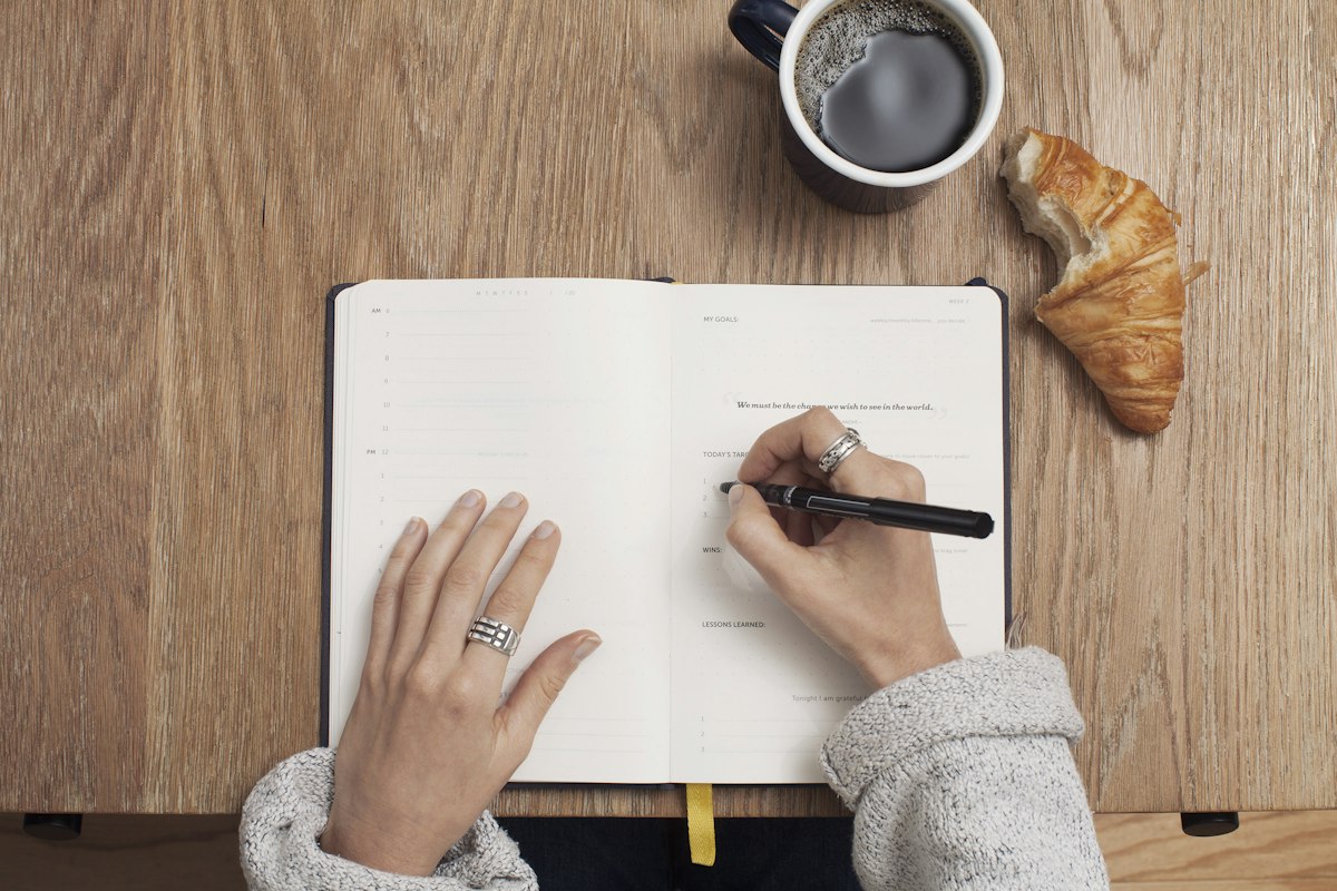 ノートに書き込む手元とコーヒーカップ