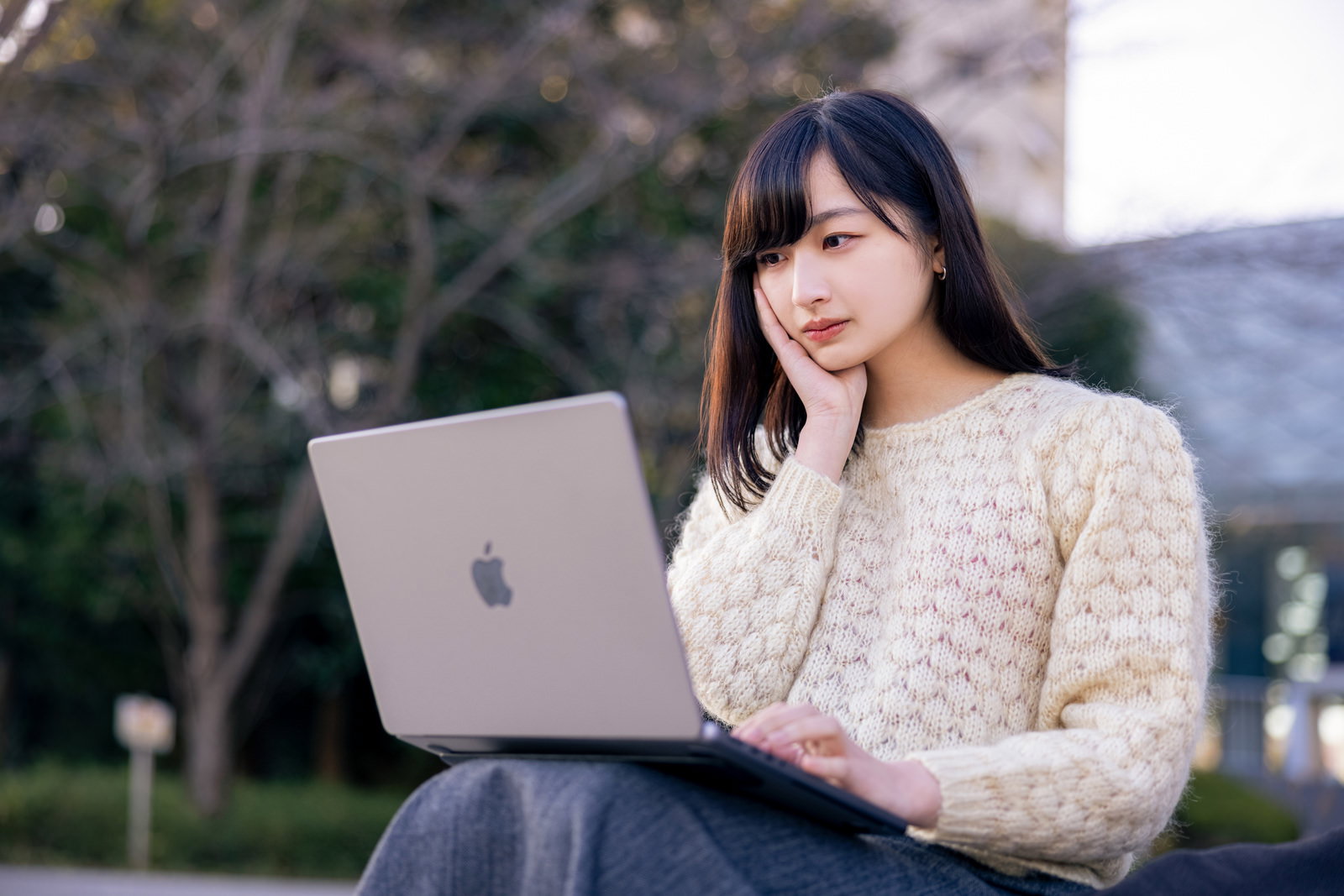 屋外でノートパソコンを前に考える女性