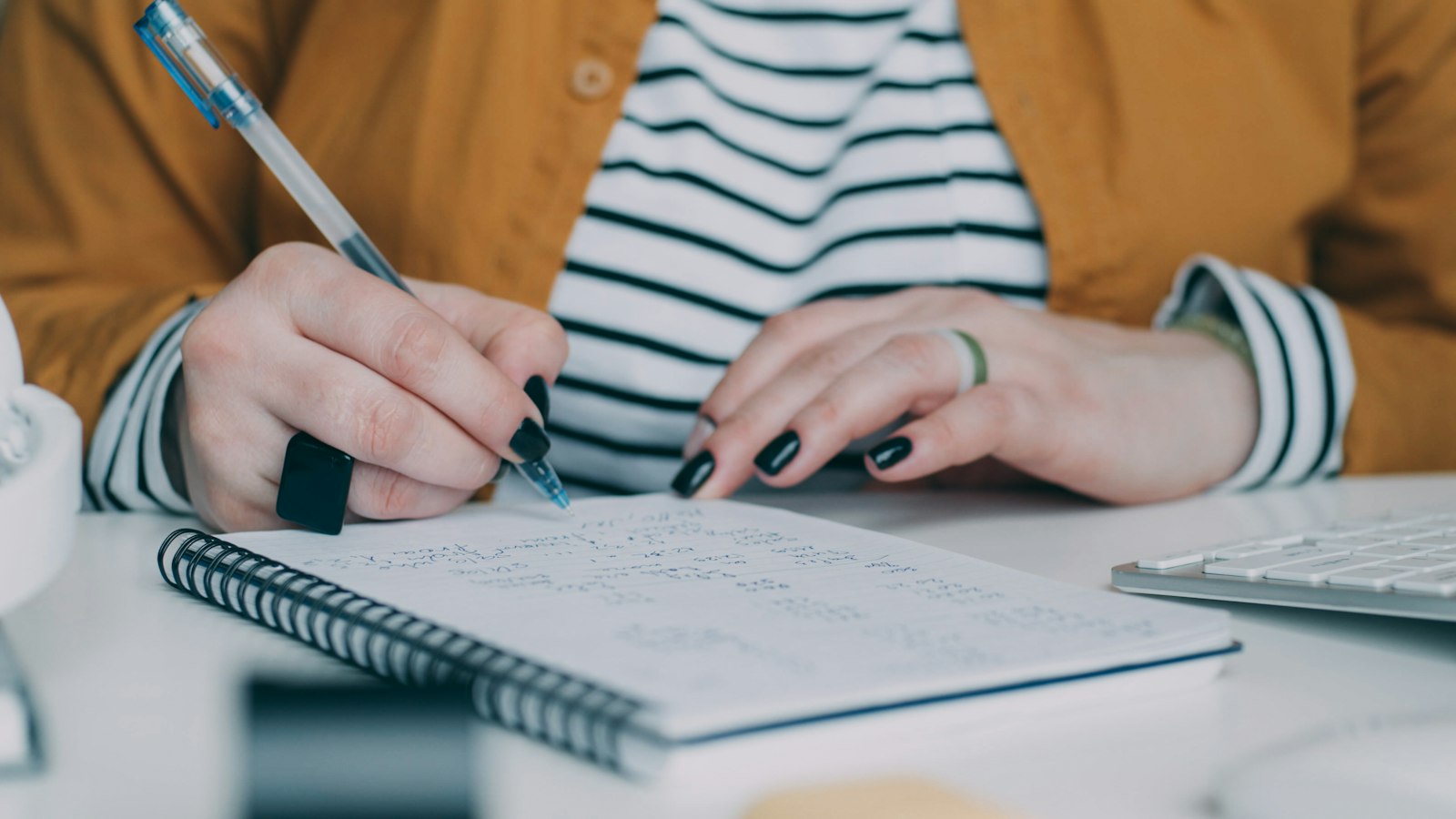 ノートに書き込みながら調べものをする女性の手元