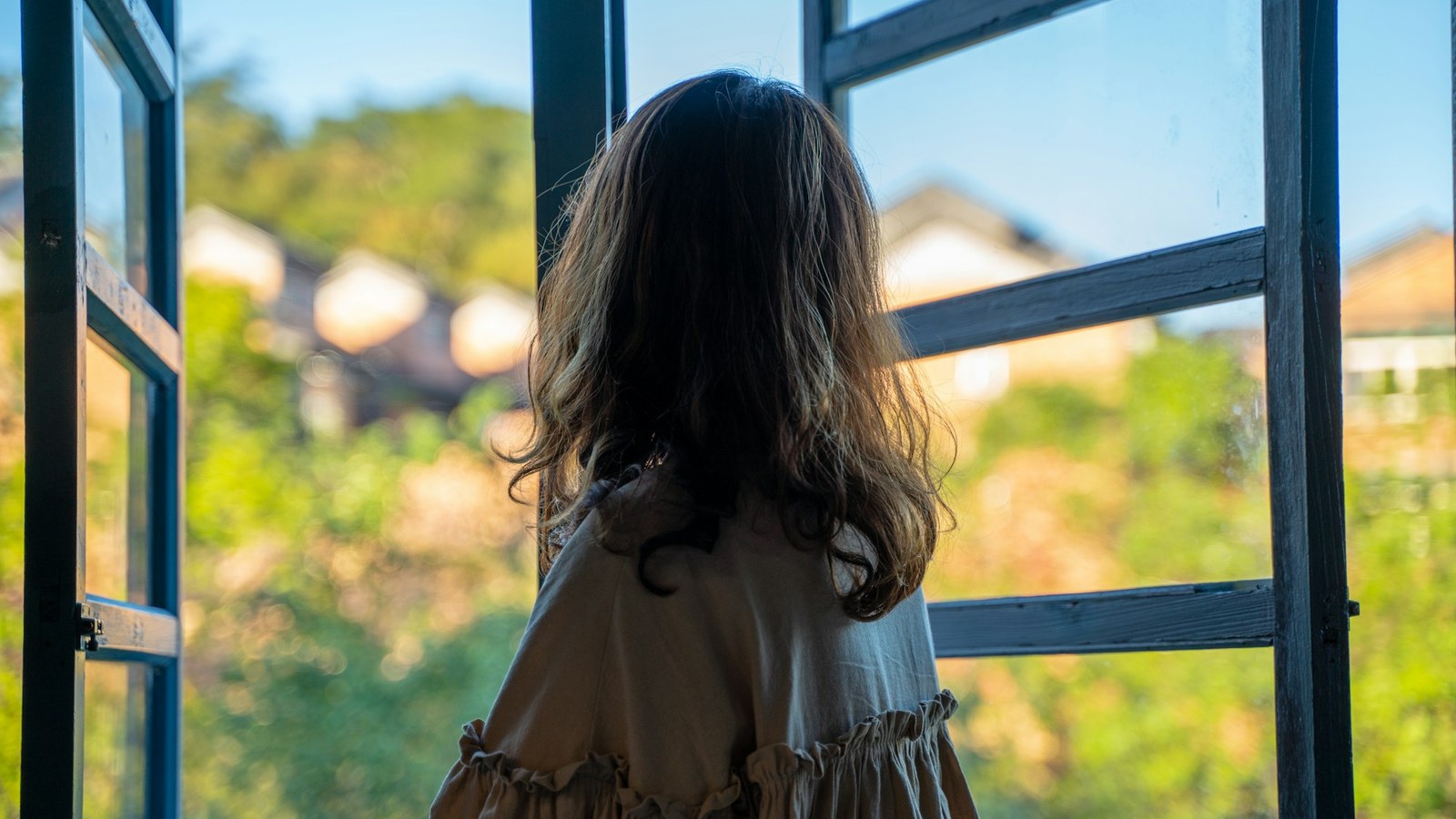 開いた窓から外を見る女性の後ろ姿