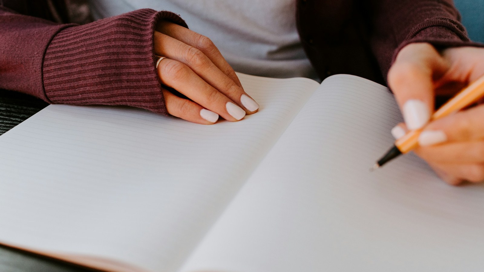 白いノートにペンで書こうとする女性の手元