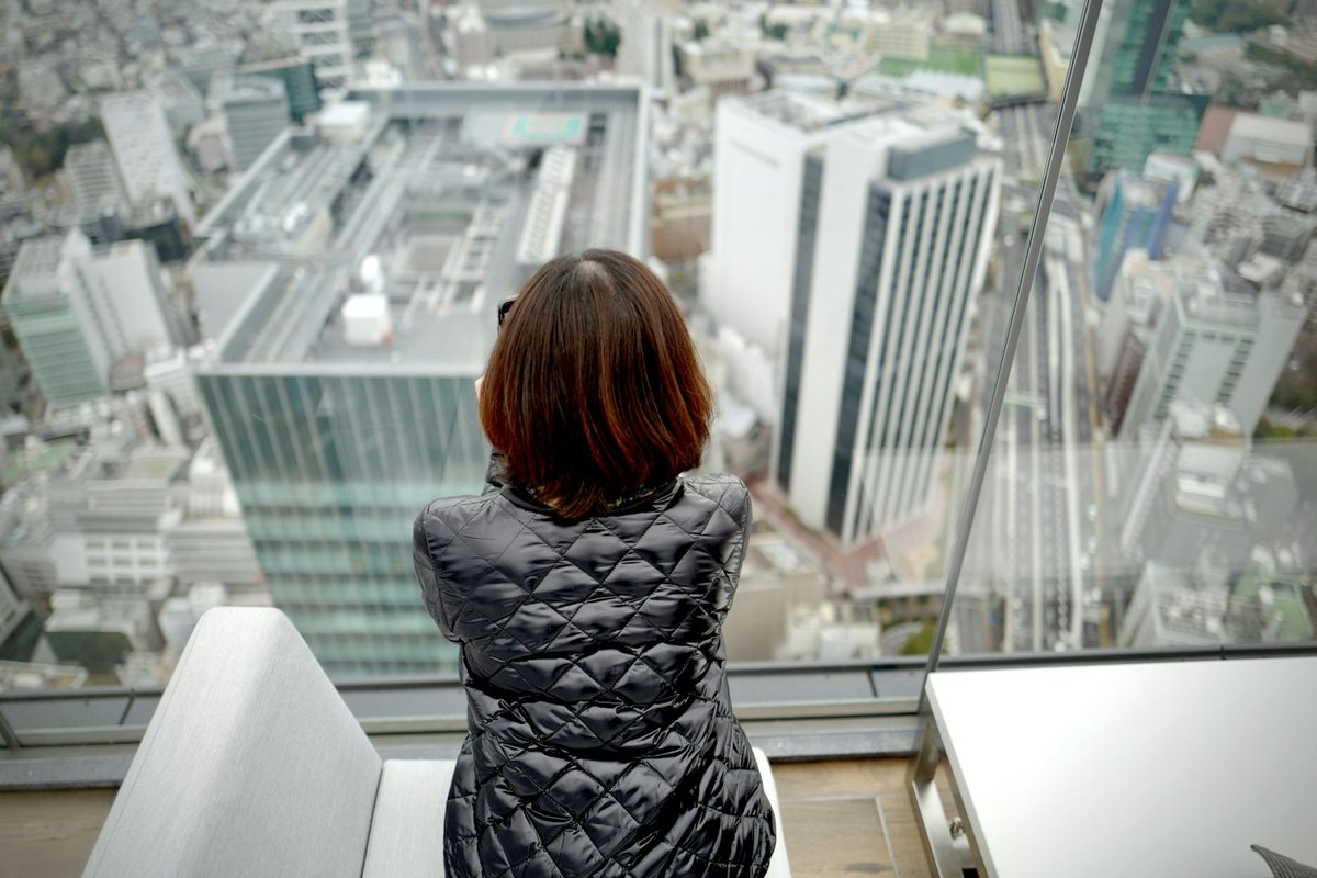 高層ビルの窓から東京の街を見下ろす女性の後ろ姿