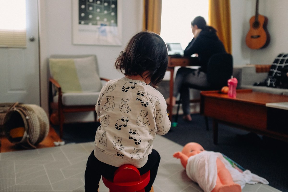 子どもが遊ぶ部屋で、奥の机で仕事をする女性