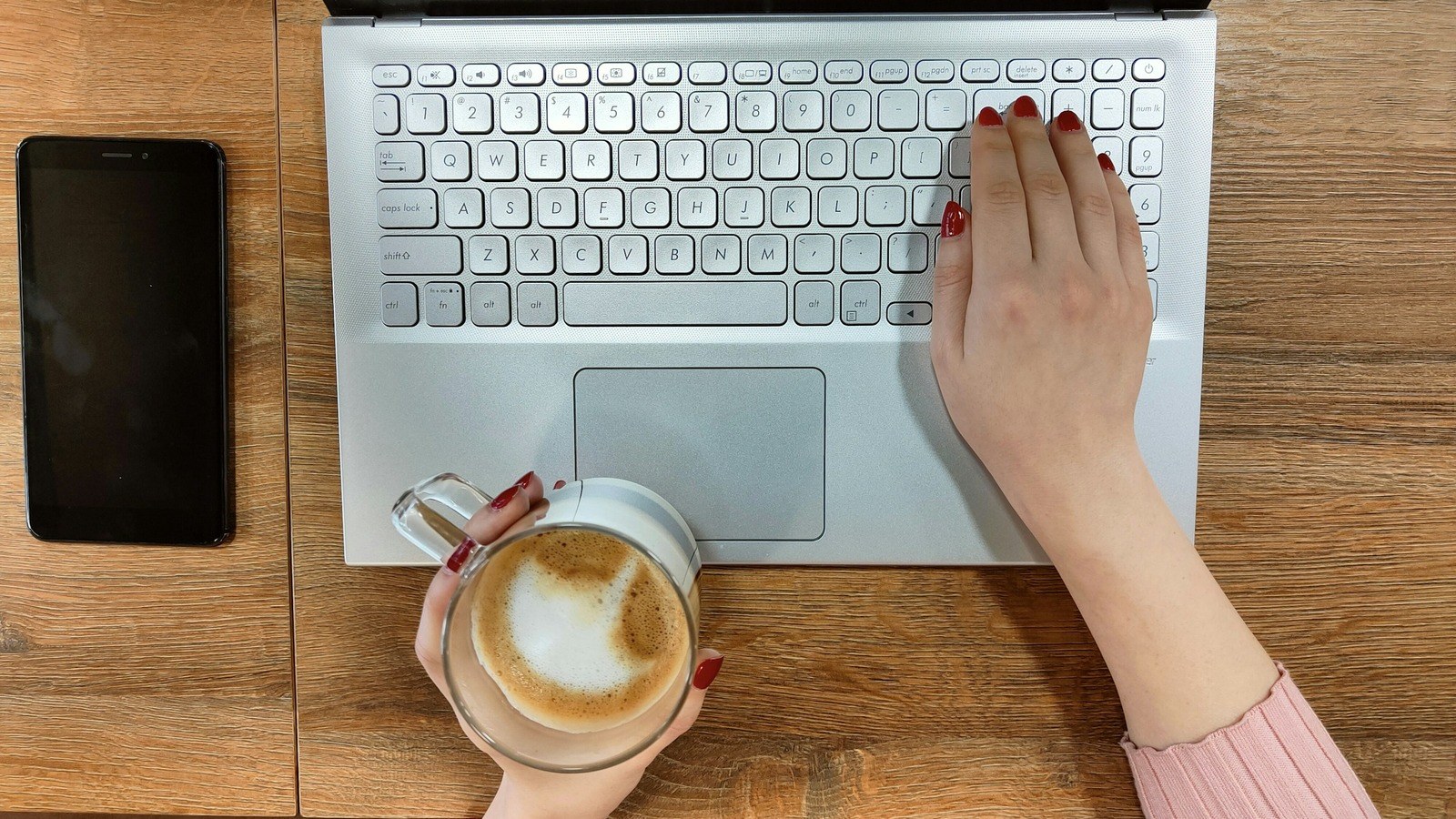ノートパソコンに手を置きカフェラテを持つ女性の手元