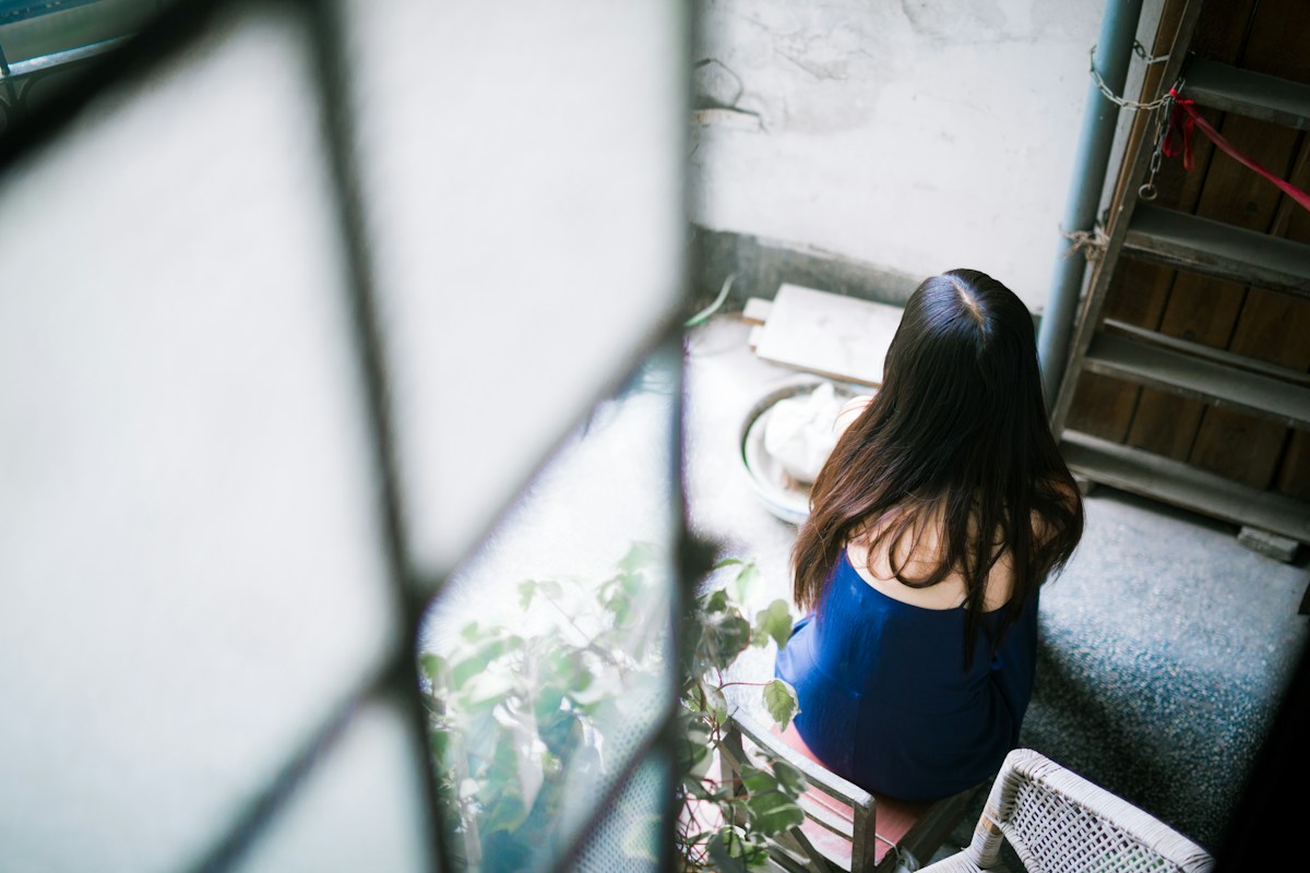 窓の外を見下ろして考える女性の後ろ姿